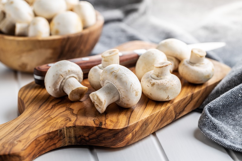 Fresh white mushrooms on cutting board.