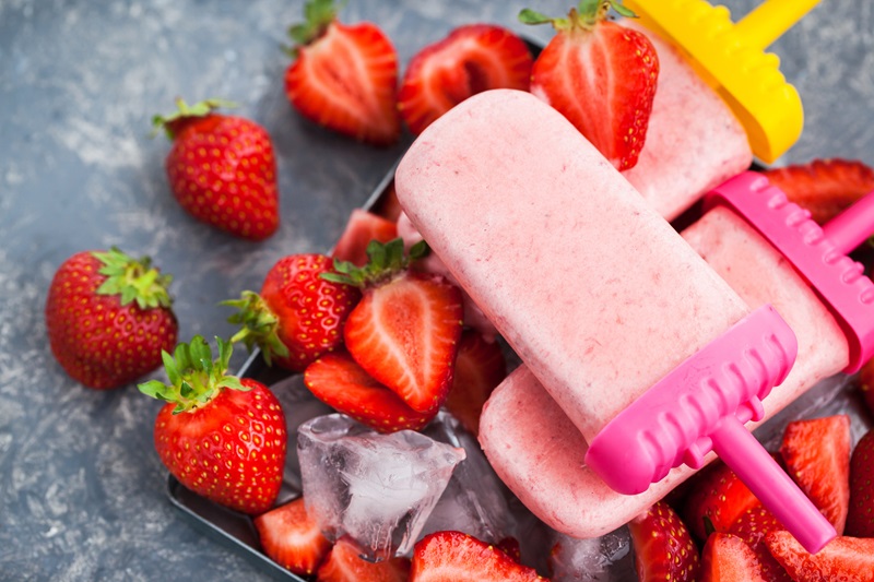 Delicious strawberry popsicles with ice and fresh berries around