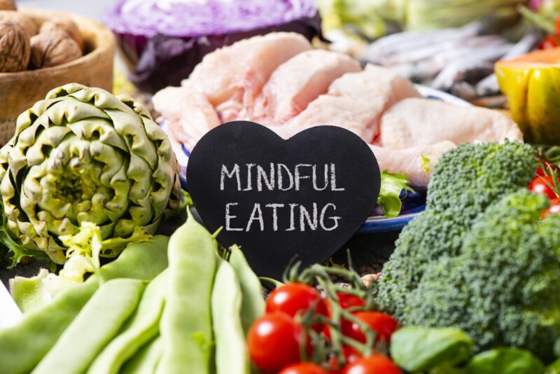 a black heart-shaped signboard with the text mindful eating, on a pile of different vegetables