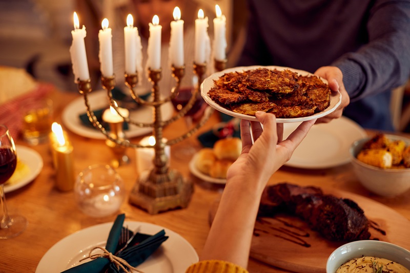 people passing latkes during a meal at dining table while celebrating Hanukkah at home.