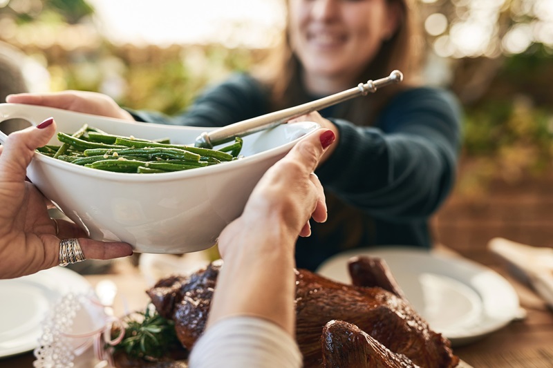 woman passing on a plate of healthy green beans over a holiday table