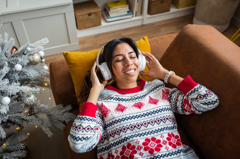 woman listening to holiday music on the couch to reduce holiday stress