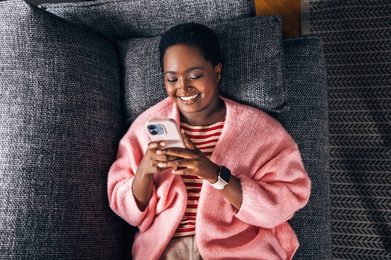 woman looking at her holiday schedule on her smart phone while laying on the couch