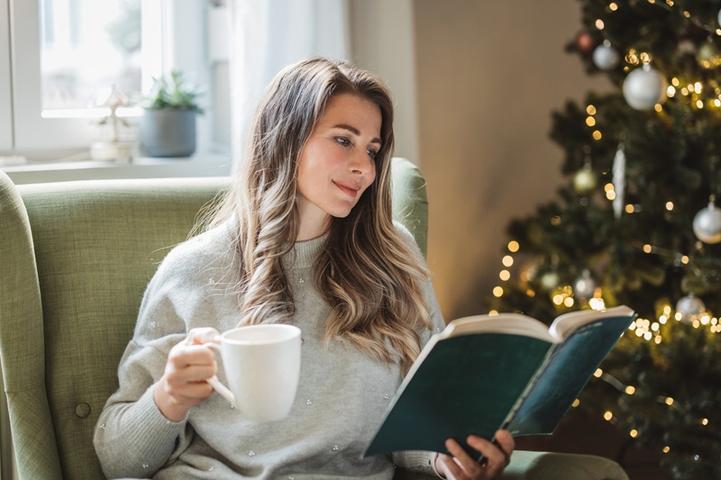 woman reading a book at home on the couch to reduce holiday stress